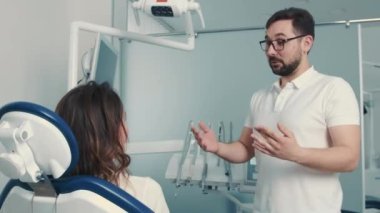 Kafkas görünümlü bir dişçi, yüz dişçi koltuğundaki bir hastayla iletişim kurar.