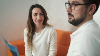 30 yaşında bir dişçi kanepede oturan beyaz bir hastayla konuşuyor ve diş röntgeni çekiyor.