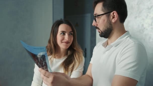 30-year-old dentist man standing talking to brunette patient on sofa and showing tooth x-ray — Stock Video