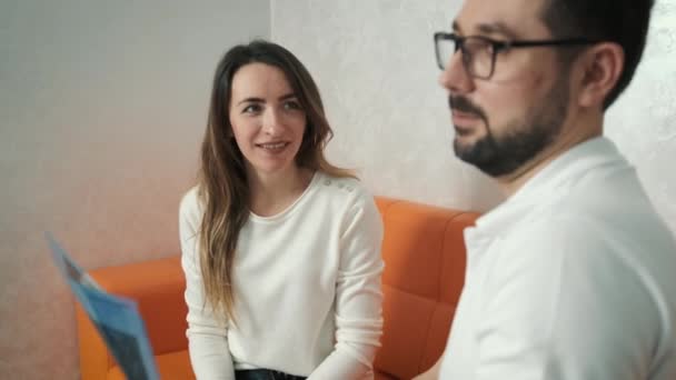 A 30-year-old dentist man sitting talking to a Caucasian patient on the couch and showing a tooth x-ray — Stock Video