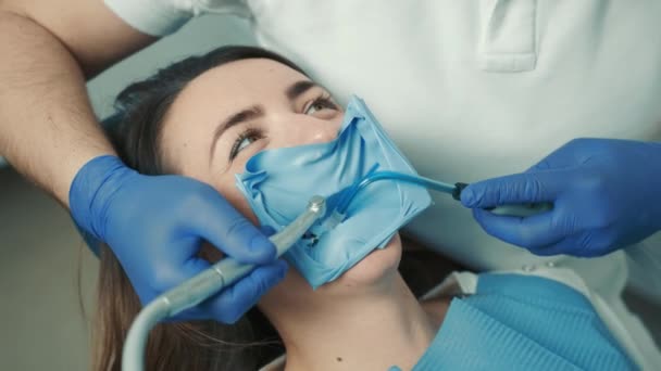Gros plan du visage d'une patiente assise sur une chaise dentaire de dentiste. Le dentiste soigne la dent — Video