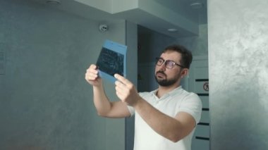 30 yaşında beyaz bir dişçi ışığın yanında duruyor ve hastaların röntgenlerine bakıyor.