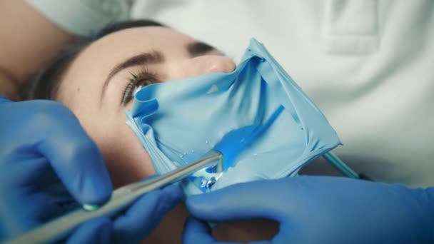 Nahaufnahme des Gesichts einer Patientin, die auf einem Zahnarztstuhl sitzt. Der Zahnarzt behandelt den Zahn — Stockvideo