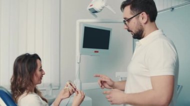 Diş kliniğinde çalışan bir erkek dişçi bir modelde hastaya dişlerini nasıl fırçalayacağını gösteriyor. Güzel gülümseme