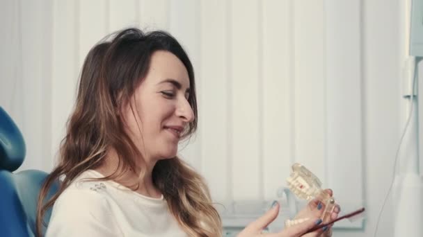 Portrait Of Woman Holding Jaw Model And Toothbrush Sitting At Dentist At Dental Care Consultation Reception — Stock Video