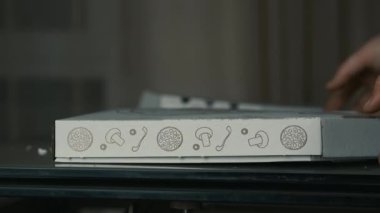 Pizzanın kutusunu yırtan bir elin yakın çekimi.