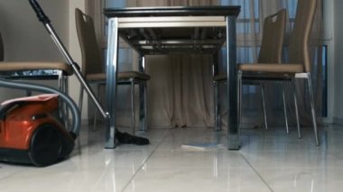 Masanın altındaki kiremitlerin tozunu temizleyen elektrikli süpürgenin yakın çekimi.