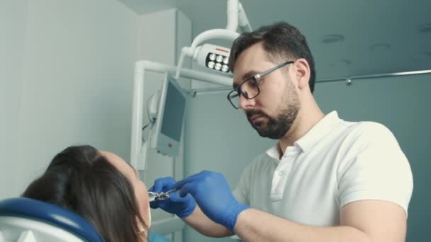 Primer plano de la cara de una paciente sentada en una silla dental. El dentista trata el diente — Vídeos de Stock