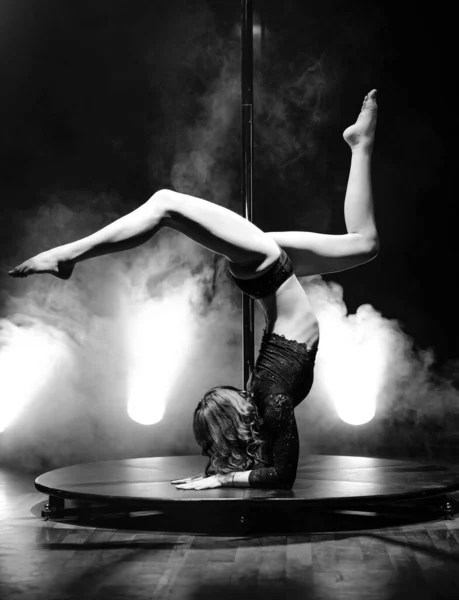Sexy slender woman dancing on a pylon in the interior of a nightclub with light and smoke. Pole dance.