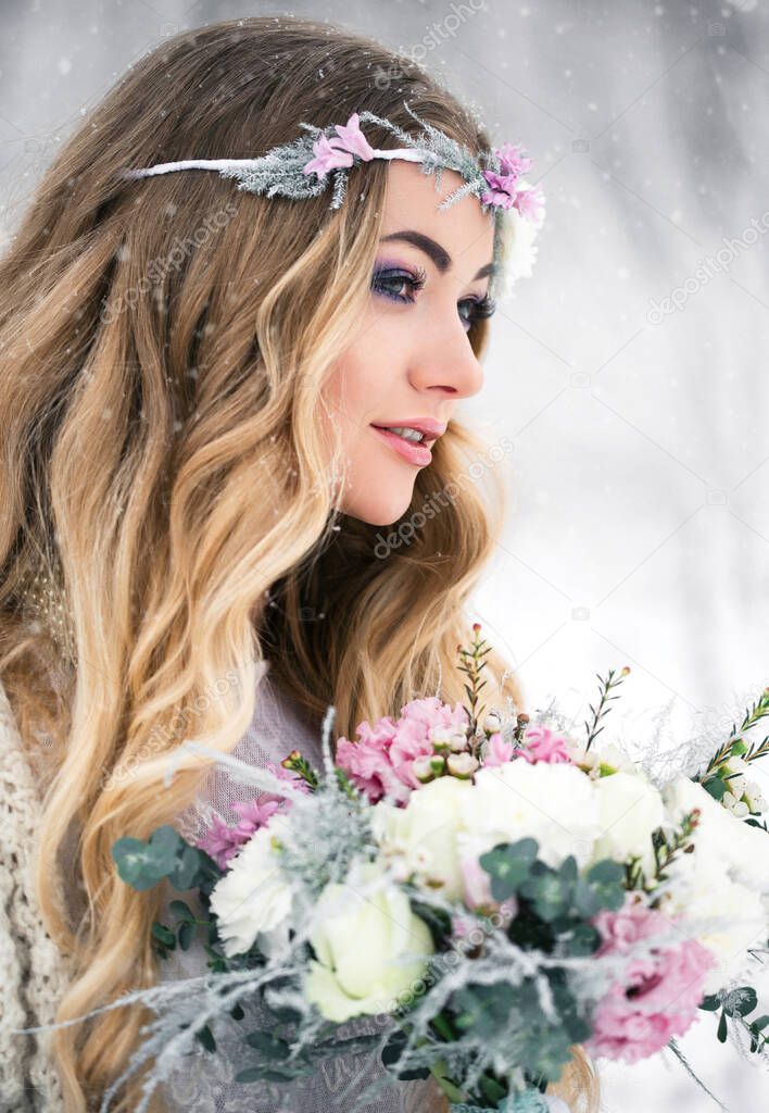 Cute bride in the winter snow forest outdoors with beautiful flowers on her head and a bouquet. The concept of a winter wedding.
