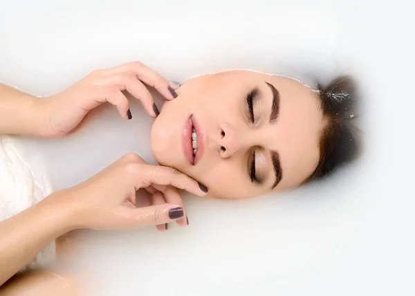 Beauty young model in a milk bath. Rejuvenation and skin care concept. A beautiful young woman with soft skin is relaxing in a milk bath.