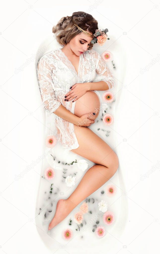A sensual pregnant woman in a milk bath with flowers. Beauty and tender motherhood.