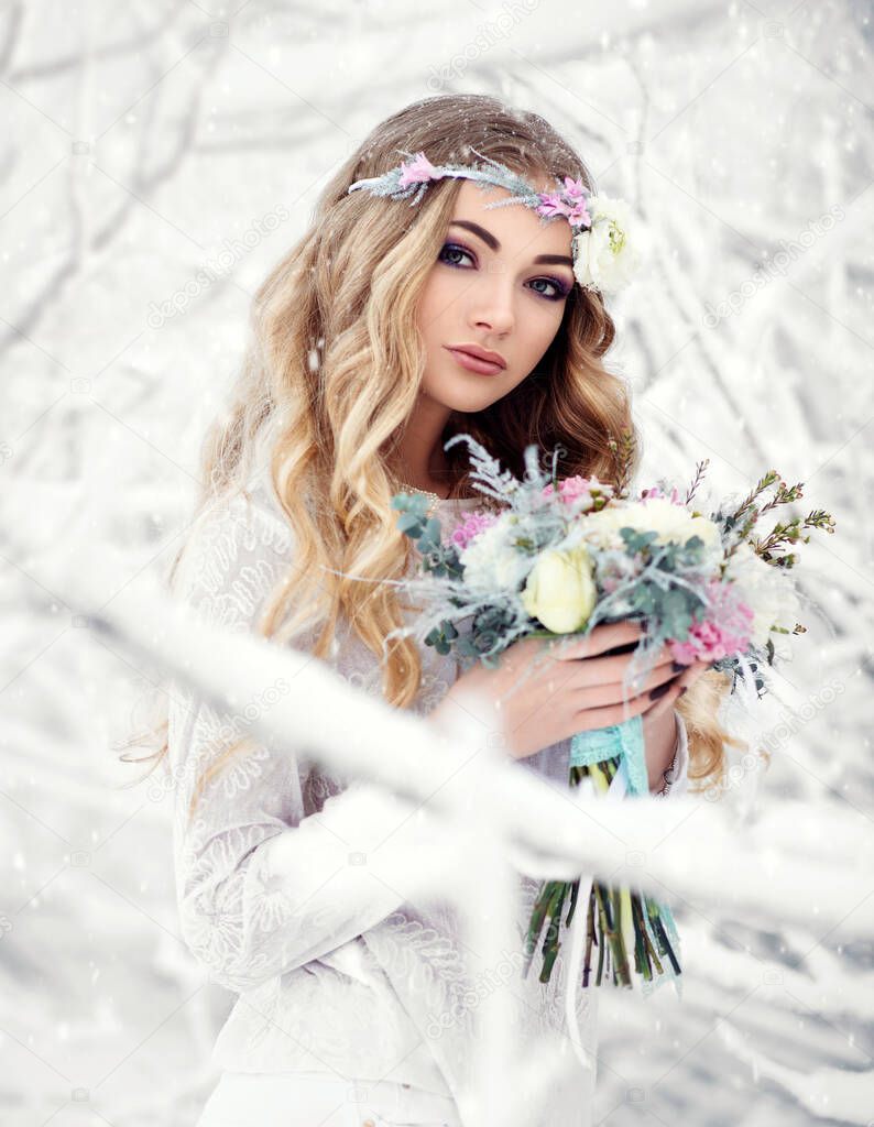 Attractive young woman in winter snow forest outdoors with beautiful flowers on her head and bouquet.