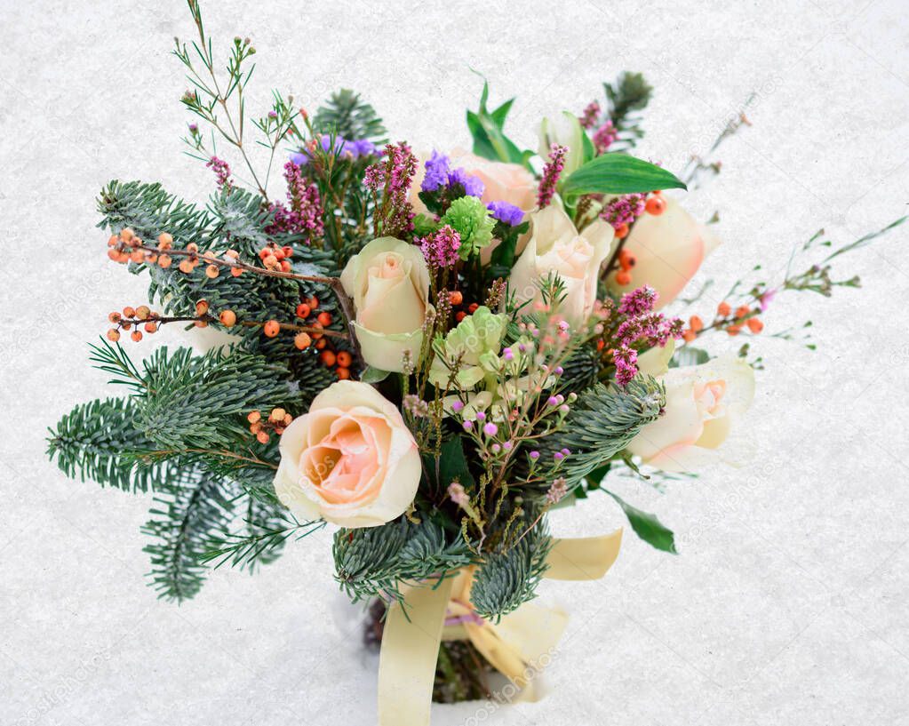 Winter wedding bouquet of roses and Christmas tree branches in the snow.