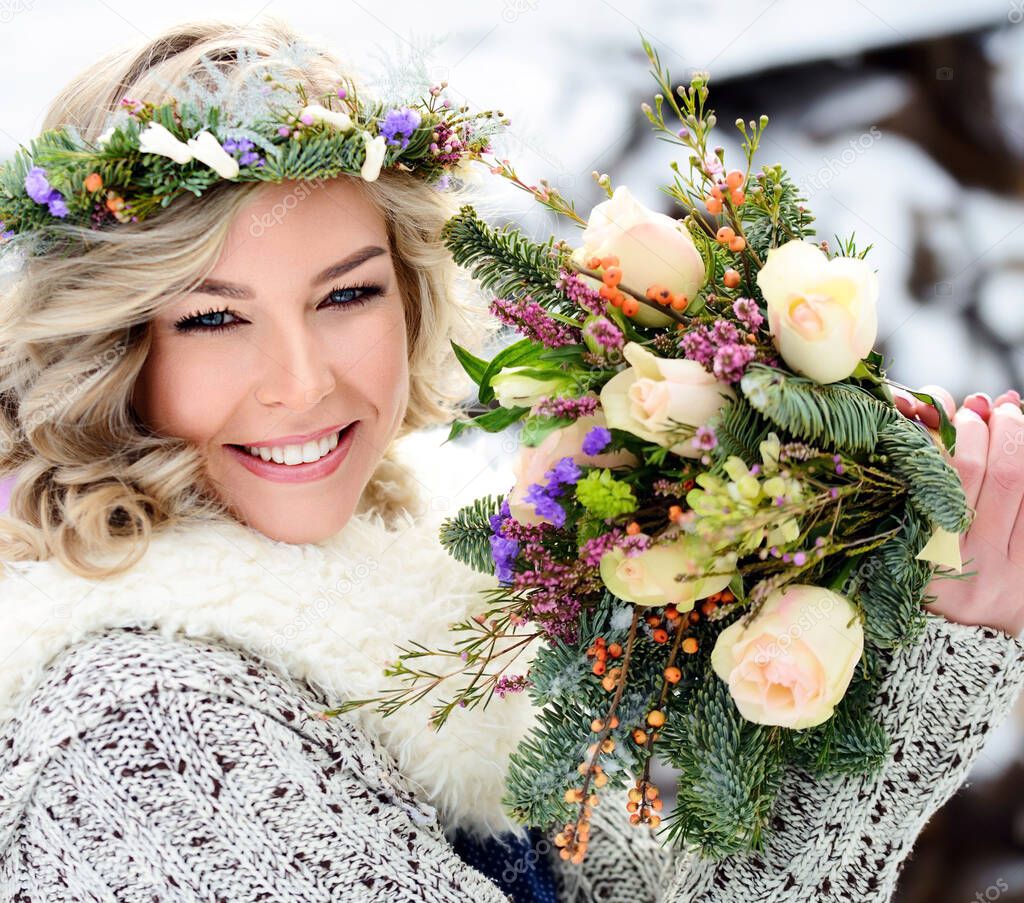 A beautiful woman with white teeth and a perfect smile holds a bouquet of roses and fir branches. Happy sincere winter outdoor portrait.