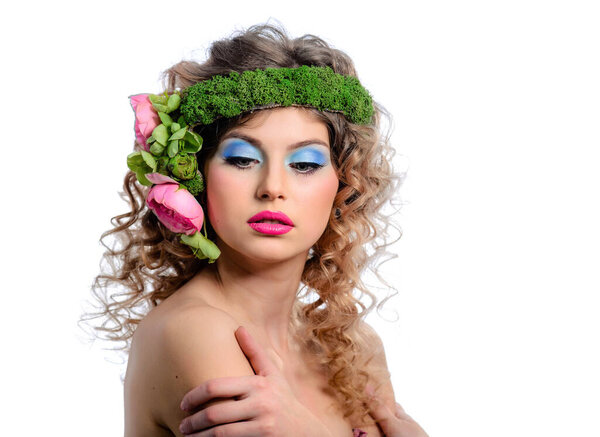 Beautiful young model with bright makeup and flowers in a curly hairstyle. Blue eye shadow and red lipstick.