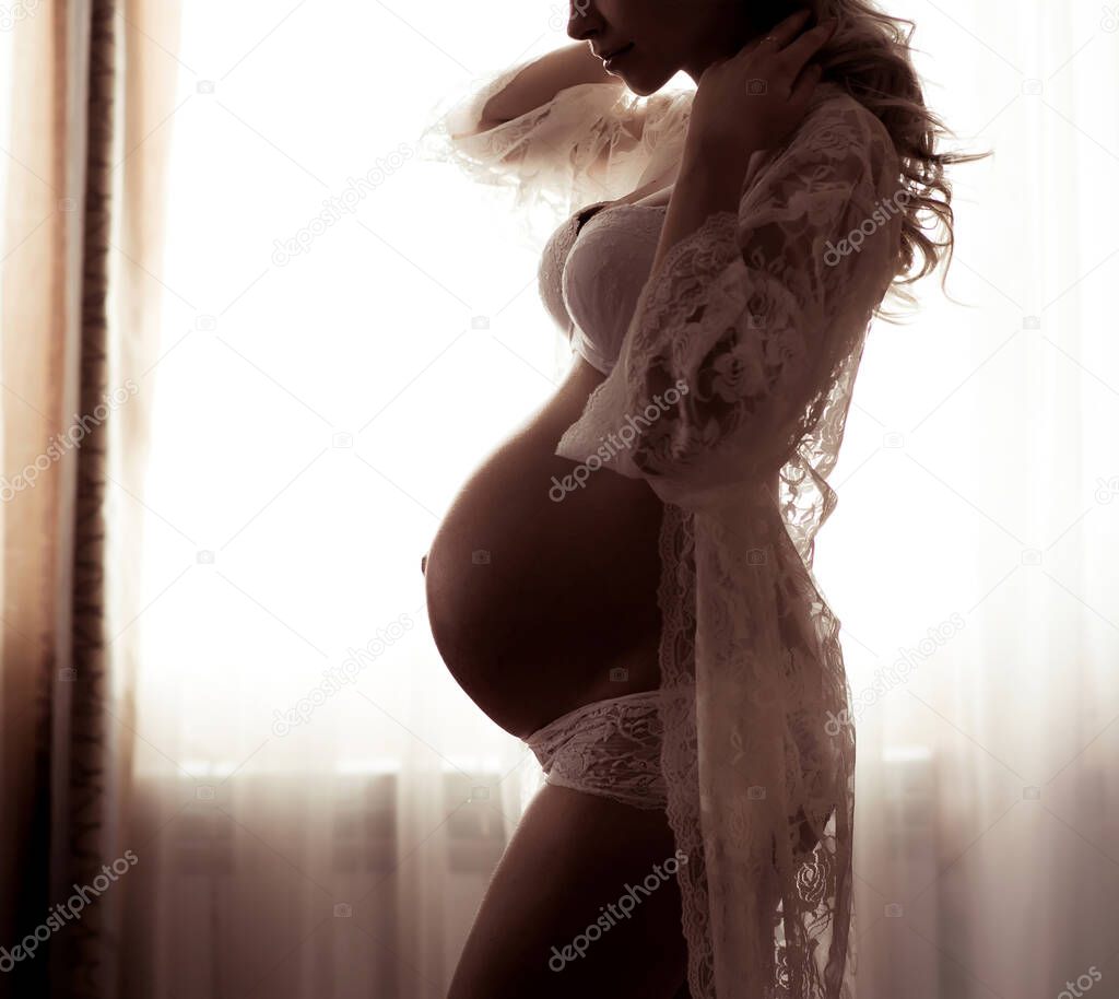 Beautiful silhouette of a pregnant woman with a belly in the ninth month. Beauty and tender motherhood. Tinted image with soft blur.