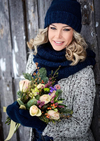 A beautiful winter woman with a perfect smile holds a bouquet of roses and fir branches. Happy sincere outdoor portrait.