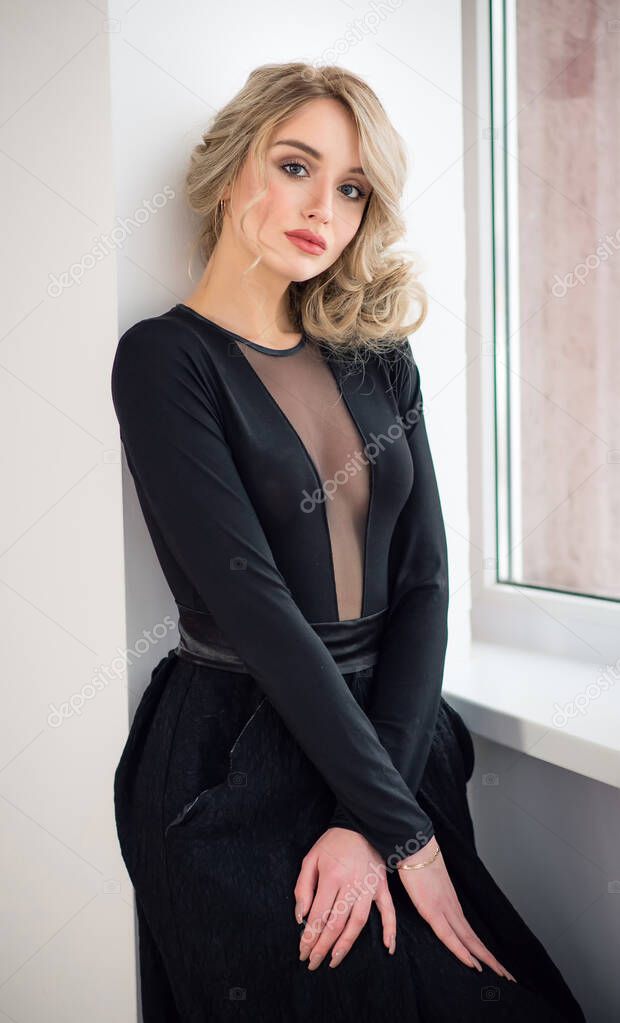 A young beautiful slim woman in a black evening dress. Beauty portrait of a model with a hairstyle