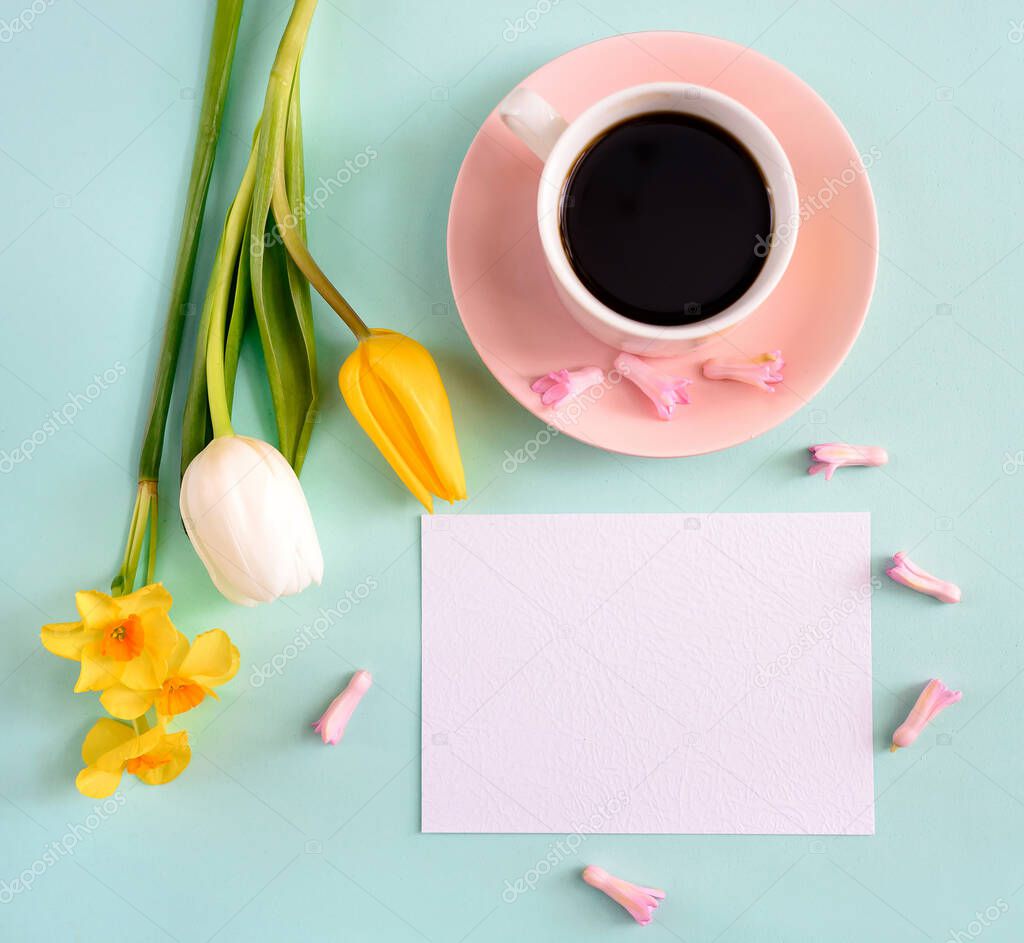 A cup of coffee and yellow tulips with empty blank on a blue background. Concept of holiday, birthday, easter, womens day. Flat lay, top view, space for text