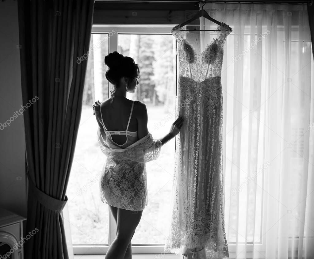 Bride morning preparation. Beautiful bride in white wedding negligee and veil near the window. Tender morning of the bride
