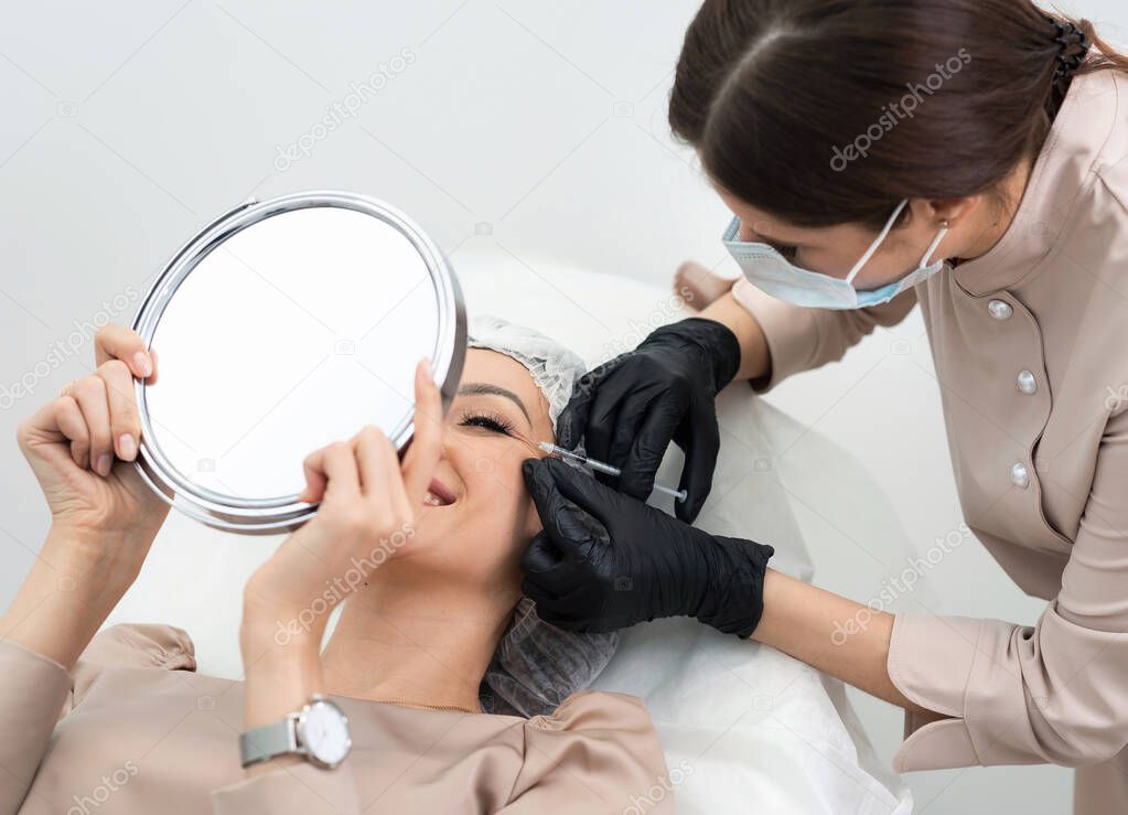 Cosmetologist making injection in eye. Young woman gets beauty facial injections in salon. Face rejuvenation and hydration procedures. Aesthetic face cosmetology