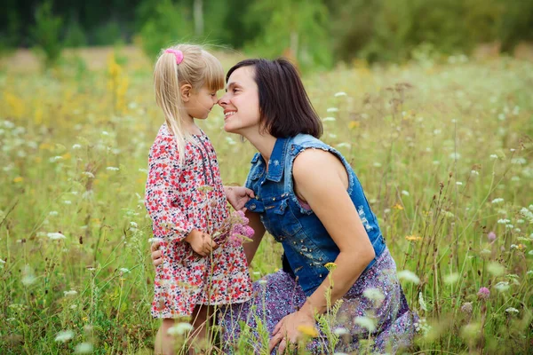 Happy mom kisses her little daughter in the summer nature. Happy people outdoor. Mothers day, love and family concept