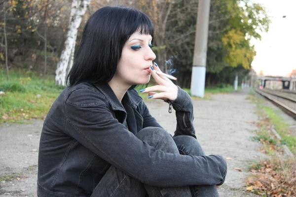 Девушка сидит и курит возле рельсов — стоковое фото