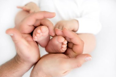 Küçük ayaklar babanın ellerinde. Baba bebeğin bacaklarını tutuyor. Kalp şeklinde podlar. Babanın ayakkabısında yeni doğmuş bir bebeğin küçük parmağı.