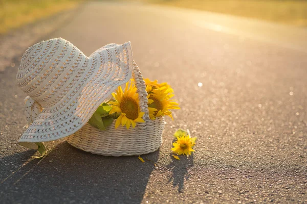 Sunflowers in a basket lie on the asphalt. Wicker hat covers a basket of flowers