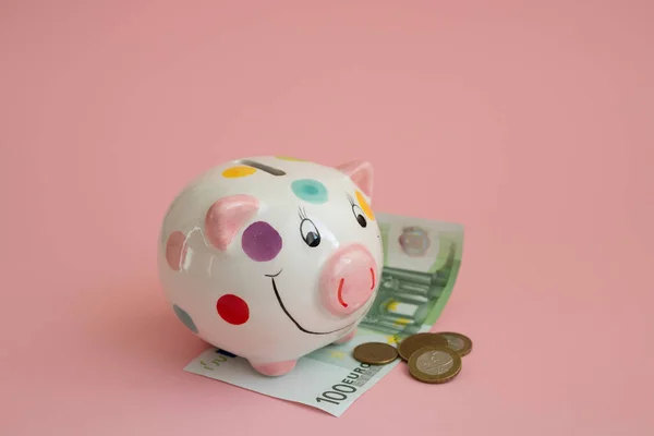 Piggy bank piggy is painted in colorful polka dots . Coins and cash on a pink background. The Belarusian ruble. Saving money and investing in the future. The currency of the euro zone.