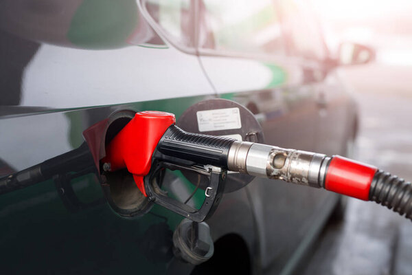 Refueling a car with gasoline or diesel fuel at a gas station. Fuel filling station. Handle fuel nozzle to refuel. A black car is being fueled by. Black car waiting for fuel tank refueling.