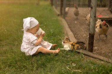Küçük çıplak ayaklı bir kız köydeki çimenlerde oturur ve bir fincandan süt içer. Kedi açgözlülükle bebeğin süt bardağına bakar. Taşrada çocukluk. Tavuklar için otlak.
