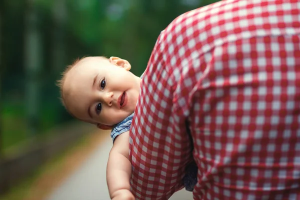 A father carries his little daughter in his arms. The child peeks out from behind Dad\'s broad shoulders. The child feels safe. The relationship between parents and children. Child psychology.