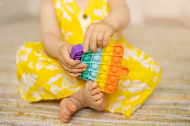 Küçük bir kız modern bir pop it oyuncağıyla oynuyor. Gelişim için büyüleyici bir duyusal oyuncak. Renkli popit oyuncağı. Çok basit. Bebek çıplak ayakla yaklaşır
