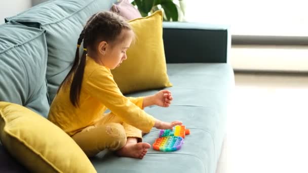 一个小女孩在玩一个现代的坑玩具 一个迷人的感官玩具 五彩缤纷的玩具 很简单的酒窝那孩子坐在沙发上 枕头是黄色的 一个令人兴奋的游戏 — 图库视频影像