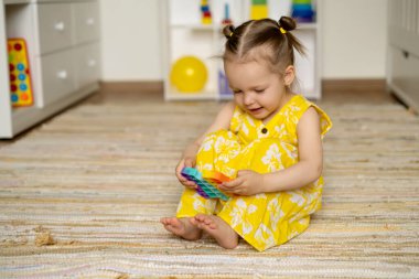 Popüler pop it oyuncağıyla çocuk odasında yerde oynayan bir kız. Motivasyon geliştirmek için bir oyuncak. Güzel motor beceriler geliştirmek için. Bir çocuk elinde bir oyuncak tutuyor..
