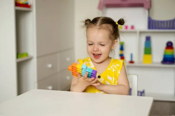 Küçük bir kız bir masada pop it oyuncağıyla oynuyor. Geliştirmek için büyüleyici bir duyusal oyuncak. Renkli popit oyuncağı. Basit bir gamze. Kız oyuncaklara tutkulu. Kahkaha ve eğlence.