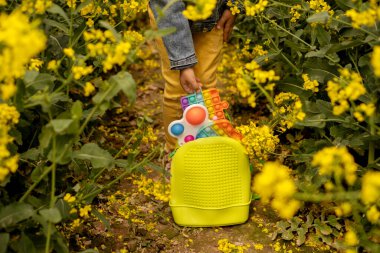 Çocuk sırt çantasından bulmaca şeklinde bir oyuncak alır. Plastik oyuncaklarla dolu bir çanta. Bir kız basit bir gamzeyle kolza tohumu tarlasında oynar ve onu patlatır.