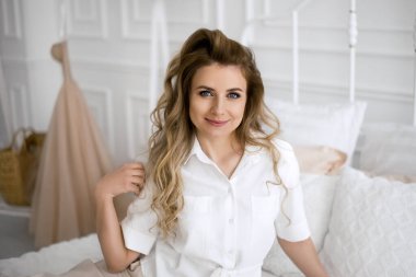 Genç, güzel, kıvırcık saçlı, anlamlı gözleri olan bir kadın yatakta oturuyor. Her gün için güzel, düzenli, günlük saç şekillendirme