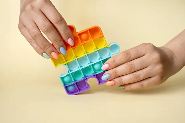 A woman holds a popular popit toy in her hands.Useful toys for the development of fine motor skills of the fingers.Anti-stress toy. entertaining games for children and adults. simple dimple.Women\'s nails of different colors. Colorful summer manicure.