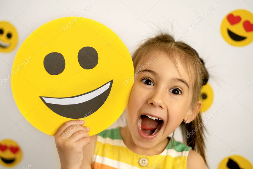 World Smile Day. Anthropomorphic Smiley Face. A little girl with a smiling cardboard smiley face is laughing out loud with her mouth open and her eyes wide and bulging in surprise. emoji day