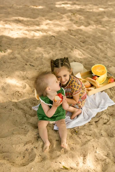 Две Сестры Песчаном Пляже Моря Весело Смеются Едят Фрукты Сладости — стоковое фото