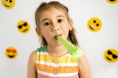 Bir kız beyaz arka planda çeşitli duygu simgeleriyle neşeli bir pipo üflüyor. Dünya emoji günü. Antropomorfik gülümseme.