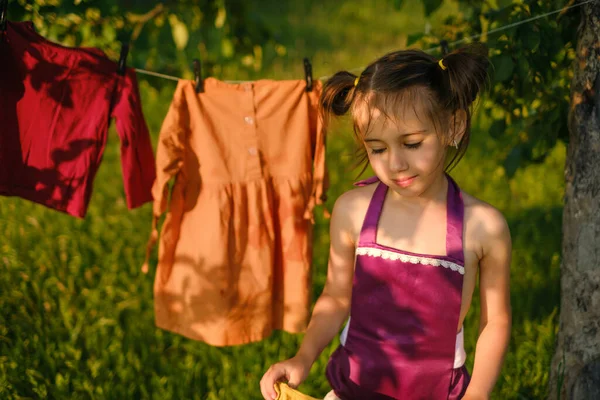 A girl carries wet clothes after washing to hang out to dry on a clothesline in the garden. Washing children's clothes with hypoallergenic safe washing powder