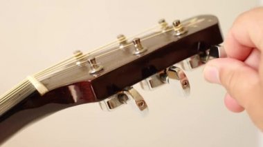 Bir kişi akustik gitarı hassas hareketlerle ayarlar. İyi bir ses elde etmek için gitar tellerinin gerilmesi gereklidir. Gitarı kendi ellerinle akort ediyorsun..