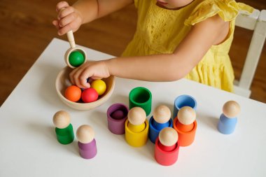 Anaokulu gelişimi için ayrıştırıcı bir oyuncak: kabın içindeki toplar. Tahta renkli figürler, toplar, kaşıklı silindirler ve renk sıralaması için bir tabak. Ellerin iyi motor becerilerinin gelişimi