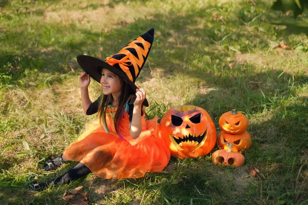 Uma Menina Bonita Está Sentada Grama Traje Bruxa Laranja Segurando — Fotografia de Stock