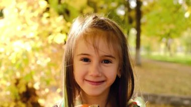 Şirin gülümseyen kız yüzünü oyulmuş bir sırıtışla şeytani bir balkabağının arkasına saklar. Cadılar Bayramı Tatili