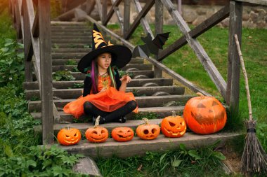 Cadı gibi giyinmiş bir kız parmak göstererek fotokopi alanını işaret ediyor. Balkabakları merdivenin basamaklarında durur. Cadılar Bayramı 'nda evin önündeki bahçeyi dekore etme geleneği..